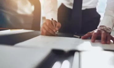 Person writing on a desk in a sunlit office.