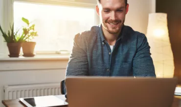 Personne souriant devant un ordinateur portable dans un bureau lumineux.