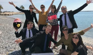 Groupe de personnes souriantes sur la plage, les bras levés.