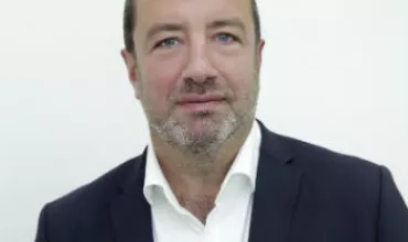 Personne en costume avec une chemise blanche, fond neutre.