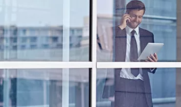 Personne en costume utilisant une tablette et parlant au téléphone dans un bureau.