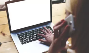 Personne utilisant un ordinateur portable et parlant au téléphone à un bureau.