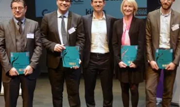 Cinq personnes en tenue professionnelle posant avec des dossiers lors d'un événement.