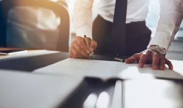 Personne signant des documents sur un bureau ensoleillé.