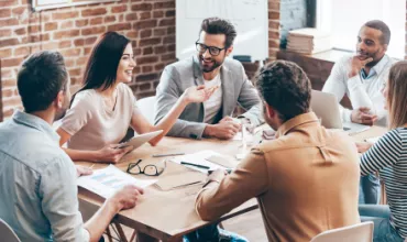 Personnes discutant joyeusement autour d'une table en bois dans un bureau moderne.