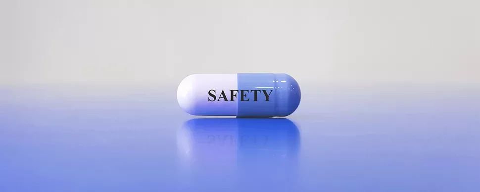 Pilule bicolore avec le mot 'SAFETY' posé sur surface bleue.