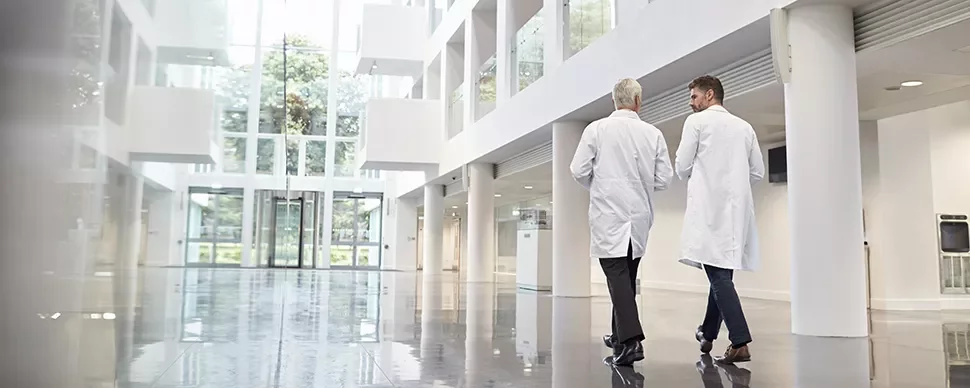 Deux personnes en blouses blanches marchent dans un hall moderne et lumineux.