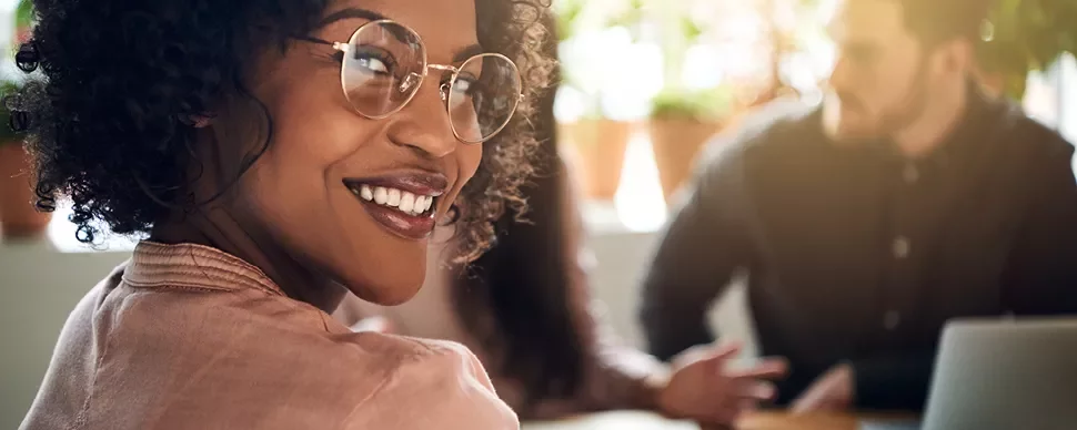 Personne souriante avec des lunettes dans un bureau lumineux.