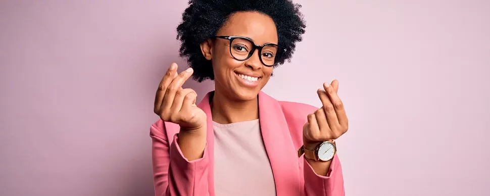 Personne souriante portant des lunettes et un blazer rose, posant devant un arrière-plan rose clair.