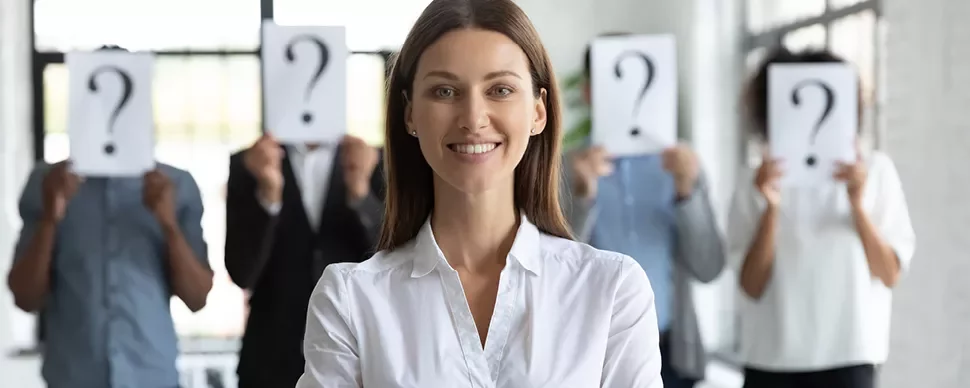 Personne souriante au premier plan, autres avec pancartes point d'interrogation en arrière-plan.