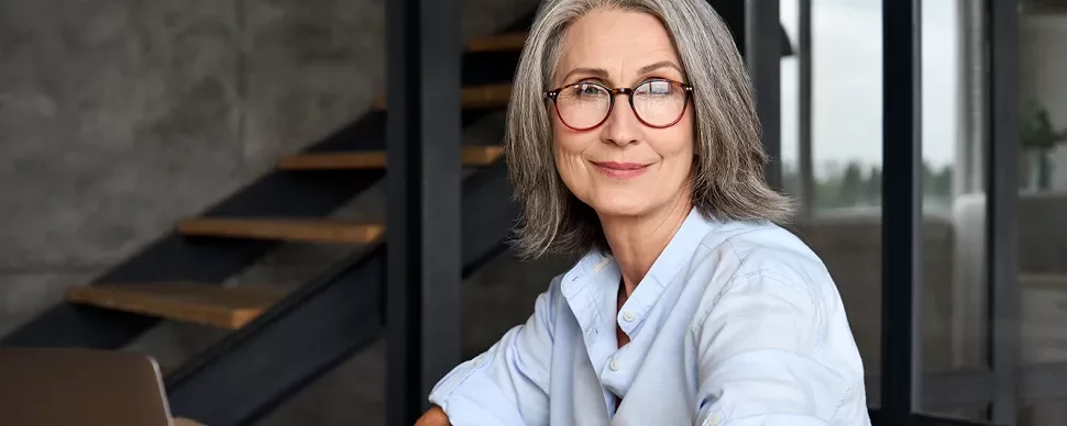 Personne souriante avec des lunettes, assise à une table.