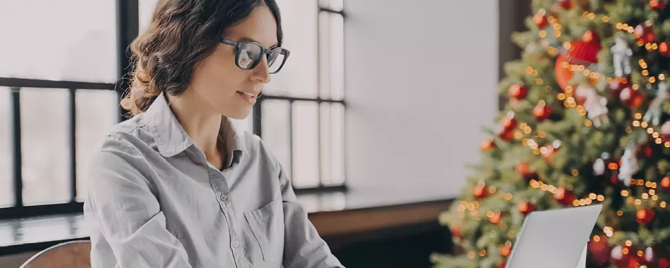 Personne travaillant sur un ordinateur portable près d'un sapin de Noël.