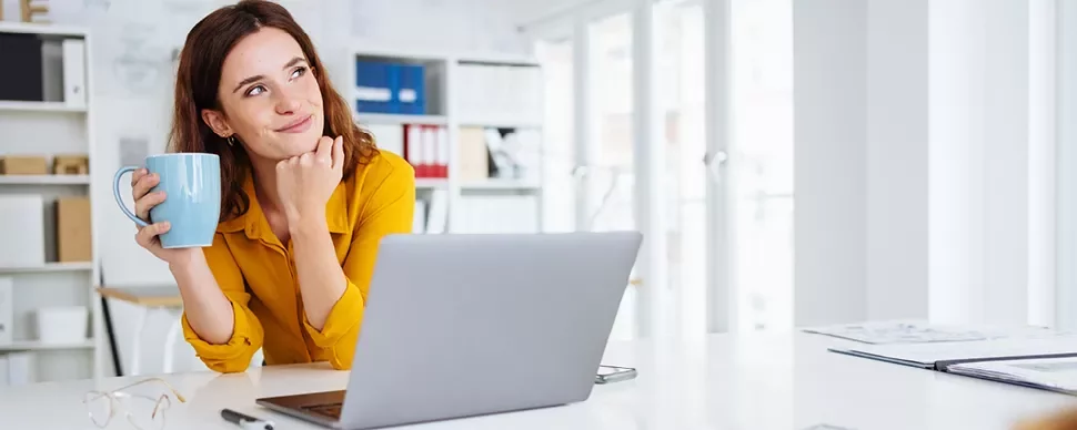 Personne tenant une tasse, rêvant devant un ordinateur portable.