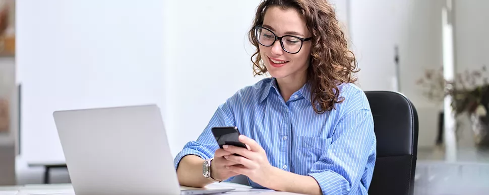 Personne souriante utilisant un smartphone devant un ordinateur portable.