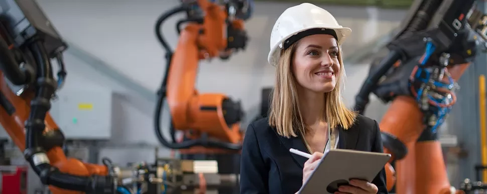 Personne avec un casque tenant une tablette dans une usine avec des robots.