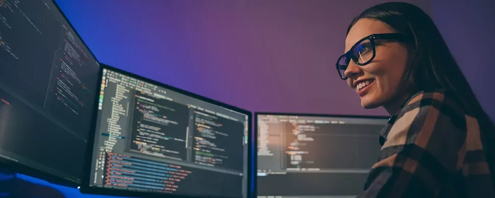 Personne souriante devant plusieurs écrans d'ordinateur avec des lignes de code.