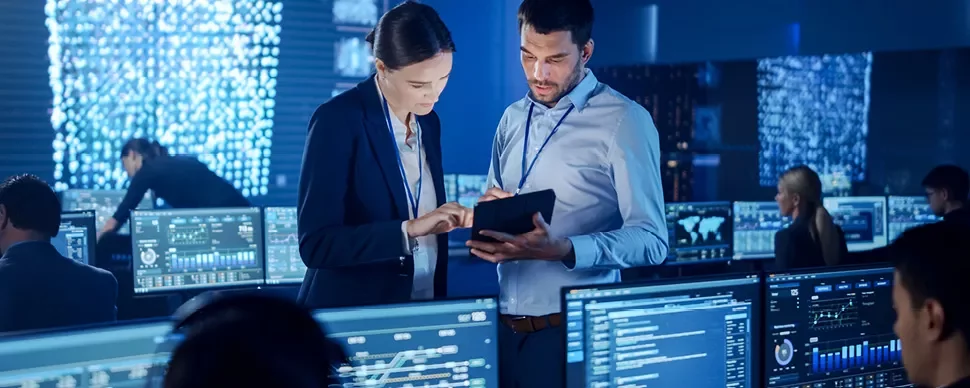 Des personnes travaillent dans un centre de surveillance informatique, entourées d'écrans affichant des données.