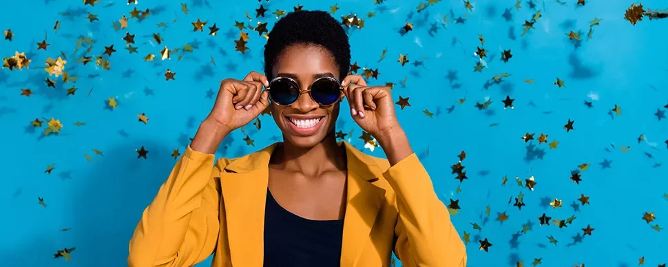 Personne souriante avec des lunettes de soleil devant un fond bleu et des étoiles dorées.