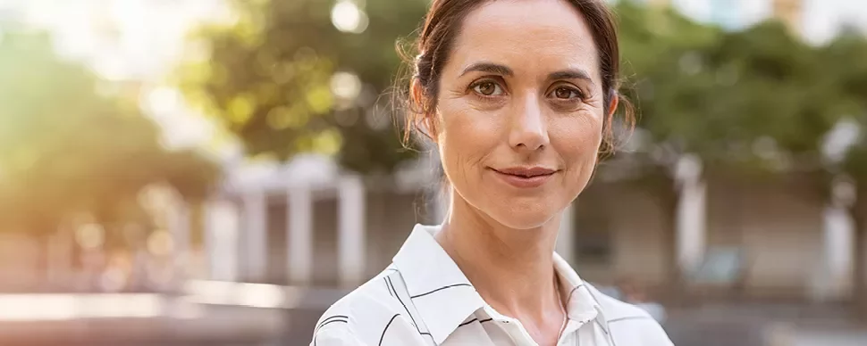 Personne souriante en chemise rayée dans un parc.