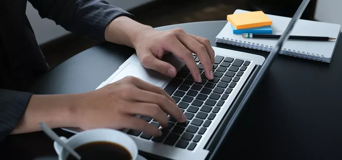 Plan rapproché sur les mains tapant sur un clavier d'ordinateur, tasse de café à côté.