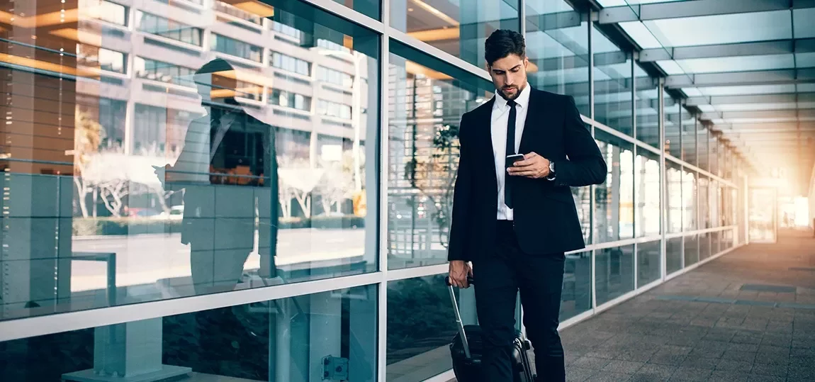 Homme regardant son téléphone tout en tirant une valise à roulette dans la rue.