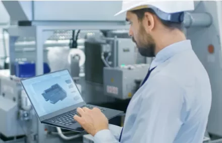 Personne en casque travaillant sur un ordinateur portable dans une usine.