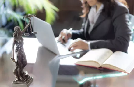 Personne travaillant sur un ordinateur portable avec une statue de justice à l'avant-plan.