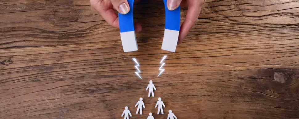 Aimant attirant des silhouettes humaines en plastique sur une table en bois.