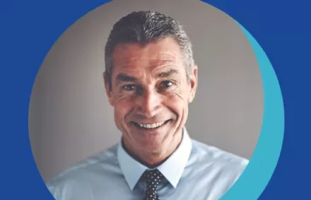 Personne souriante en chemise bleue et cravate à pois.