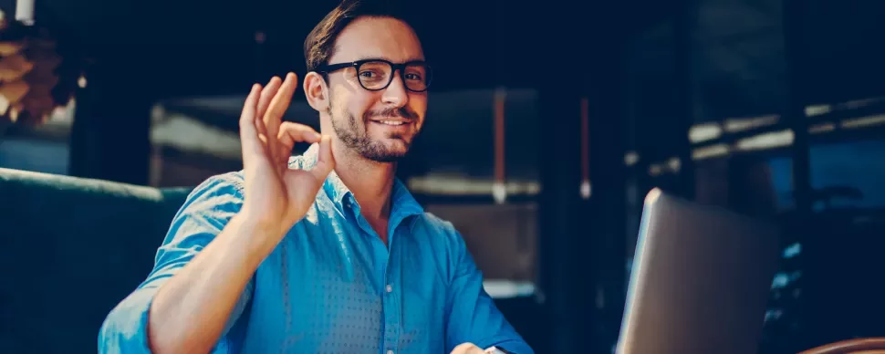 Personne souriant faisant un signe OK devant un ordinateur portable.