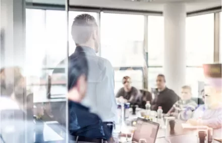 Réunion de travail dans une salle vitrée avec plusieurs personnes attentives.